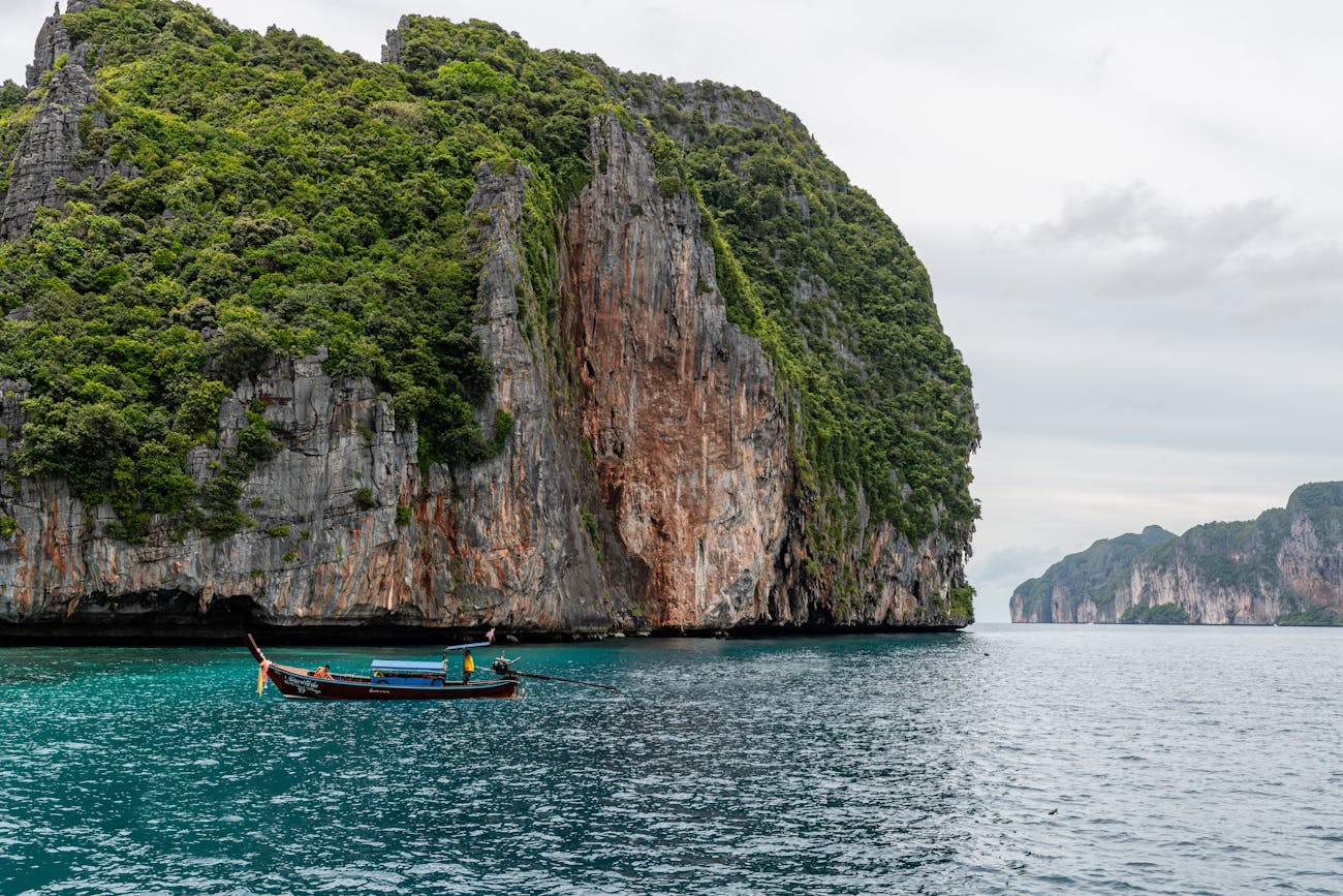 A boat passes by one of the multi-colored limestone cliffs in Phang Nga Bay, Thailand.